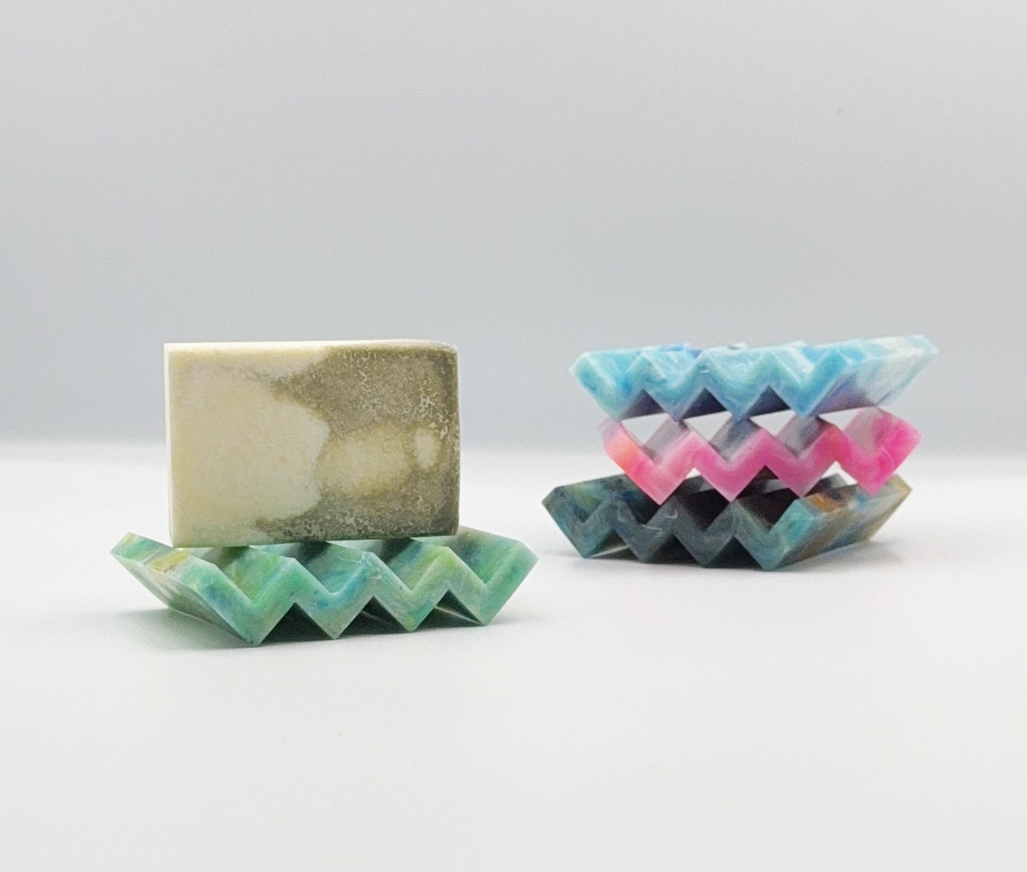 Zigzag soap dish straight on view with soap bar. 4 colours made from recyled household plastic. 3 dishes stacked in the background